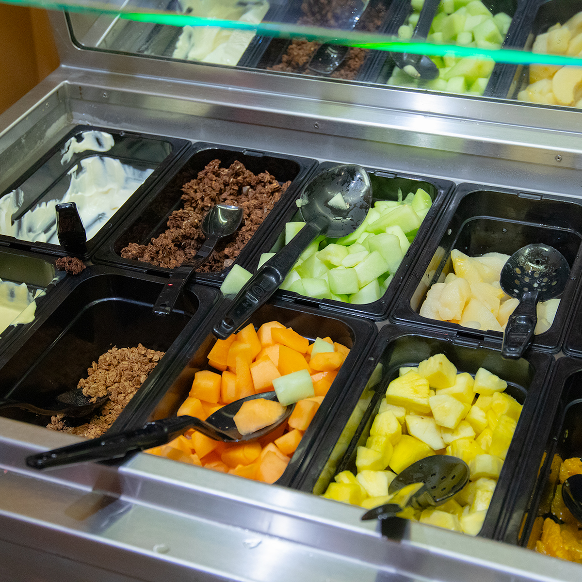 Assortment of fruit and yogurt in containers, including cantaloupe, apples, and pineapple.