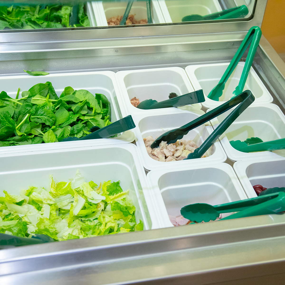 An image of vegetables in salad bar containers, including lettuce, onions, and other veggies.